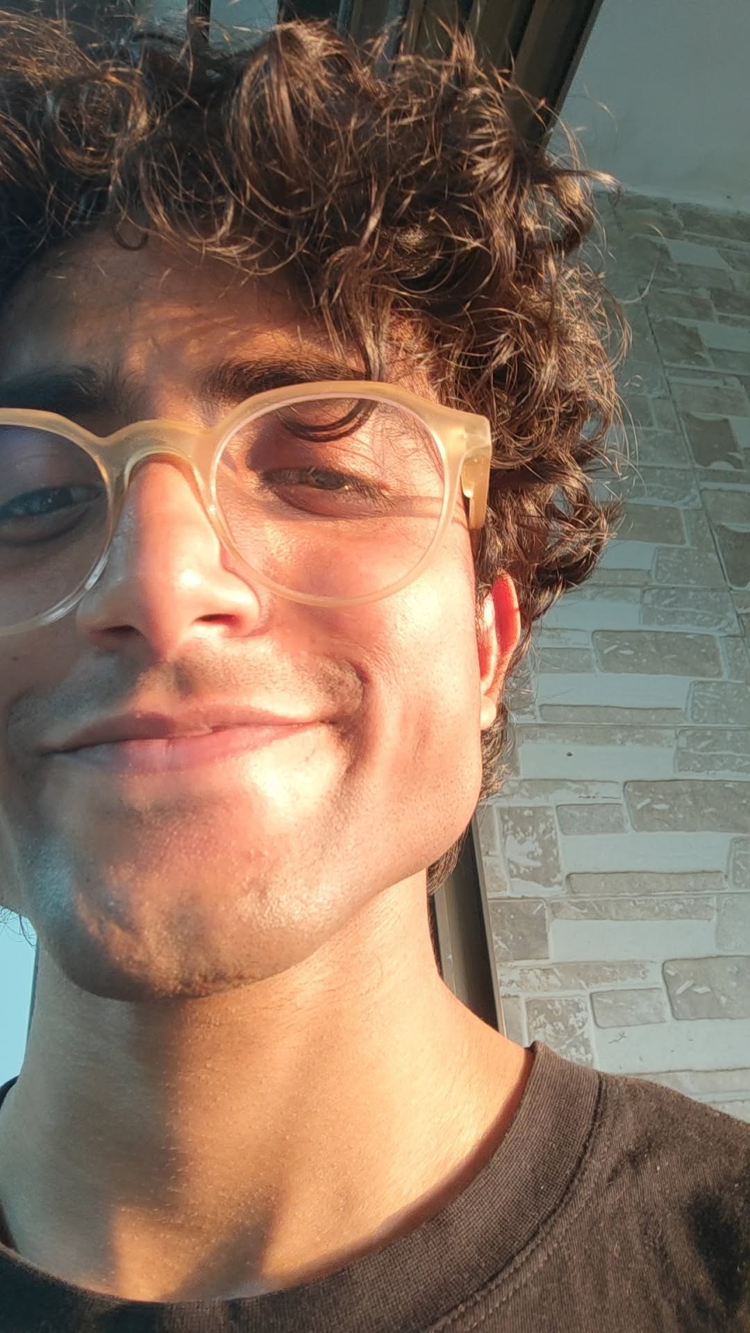Kavish smiling in evening sunlight, curly hair, clear-framed glasses