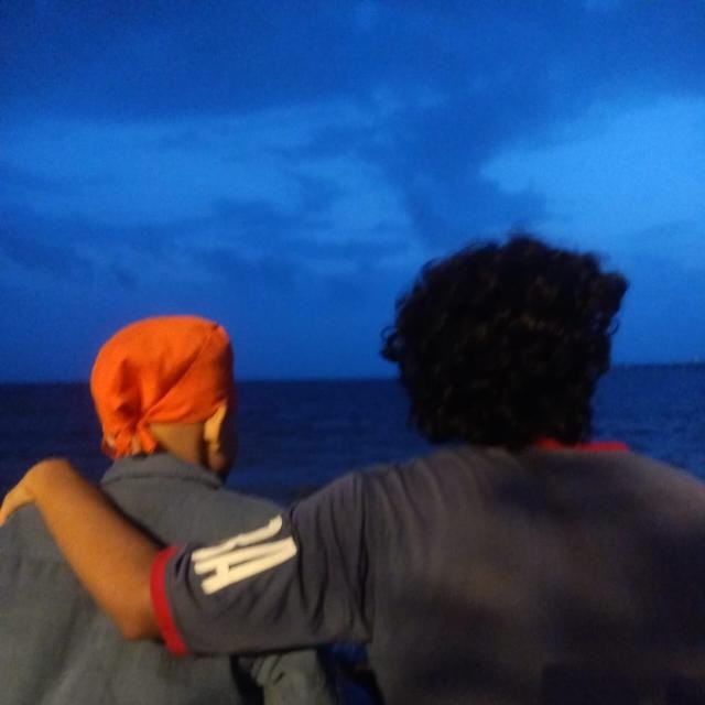 Kavish and his brother from behind, his arm around his brother, looking out at the sea at dusk